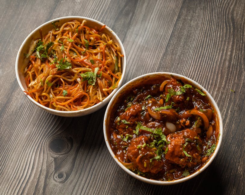 Two small bowls of Asian-inspired dishes placed on a dark wooden surface. The left bowl contains stir-fried noodles with julienned carrots, chopped green herbs, and a light soy-based sauce, showcasing